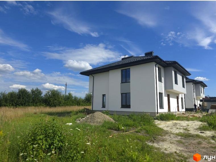 Зовнішній вигляд будинків житлового комплексу КМ Savanna з прибудинковою територією, зелена трава та облаштовані ділянки.