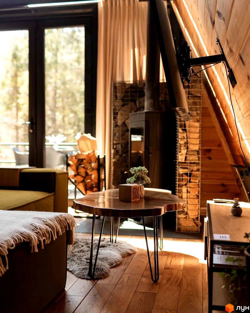Інтер'єр будинку Котеджного містечка Yahody з дерев'яними стінами, каміном та великим вікном. У кімнаті видно диван, журнальний столик та вид на ліс.