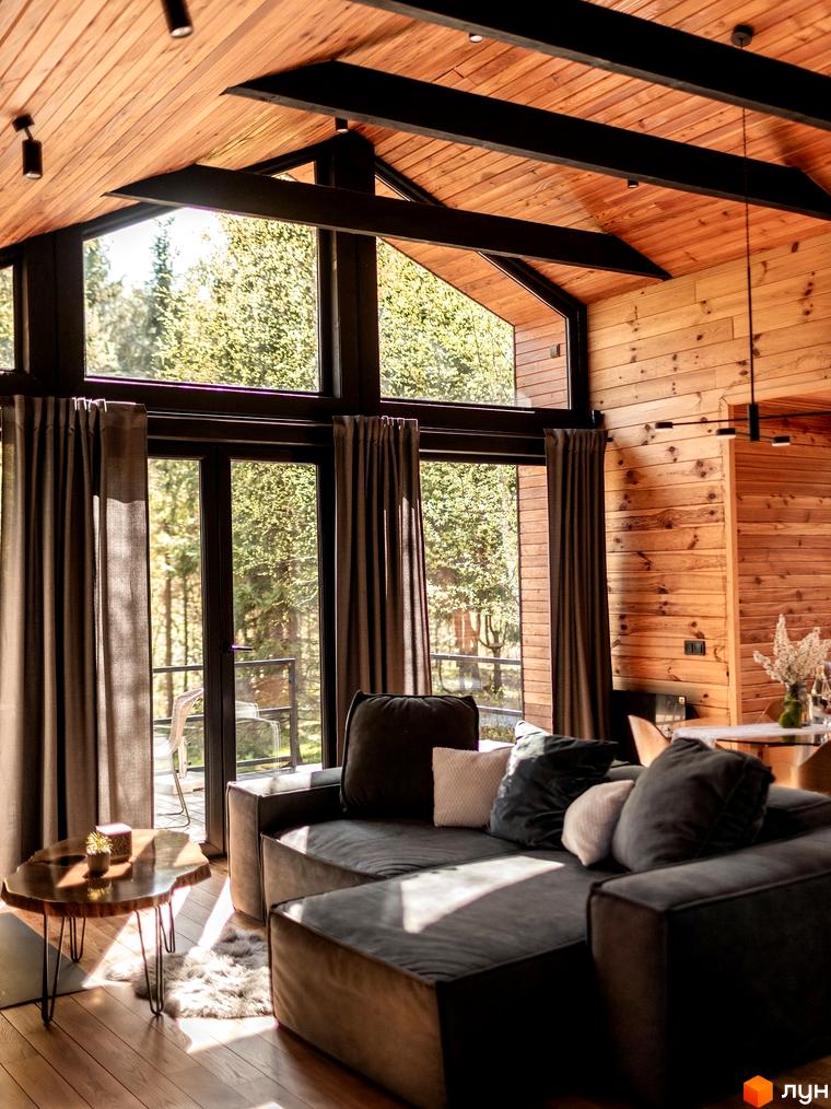 Котеджне містечко Yahody: будинок з великими панорамними вікнами, що виходять на лісову ділянку. У вітальні дерев'яні стіни та стеля.