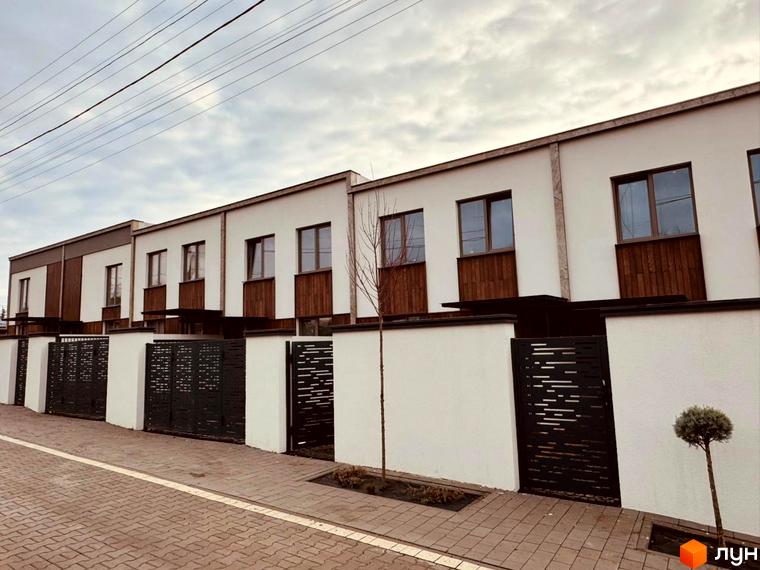 Таунхауси Luxor Gardens з білими фасадами та дерев'яними елементами, огороджені чорними парканами. Поруч бруківка та зелені насадження.