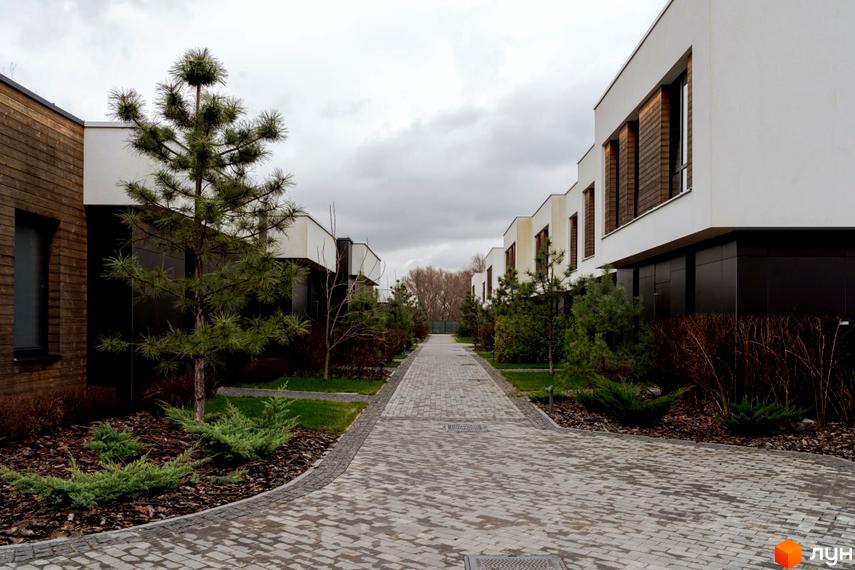 Котеджне містечко КМ YOND.City. Зовнішній вигляд будинків та доглянута прибудинкова територія з бруківкою та деревами.
