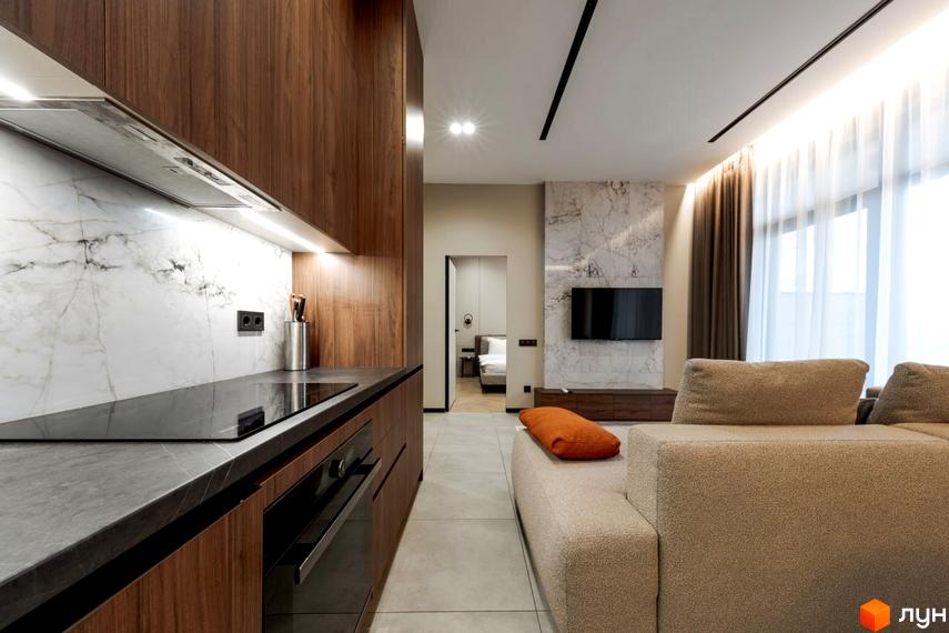 Інтер'єр квартири в комплексі КМ YOND.City: кухня з дерев'яними фасадами та мармуровим фартухом, вітальня з диваном та телевізором на мармуровій стіні.