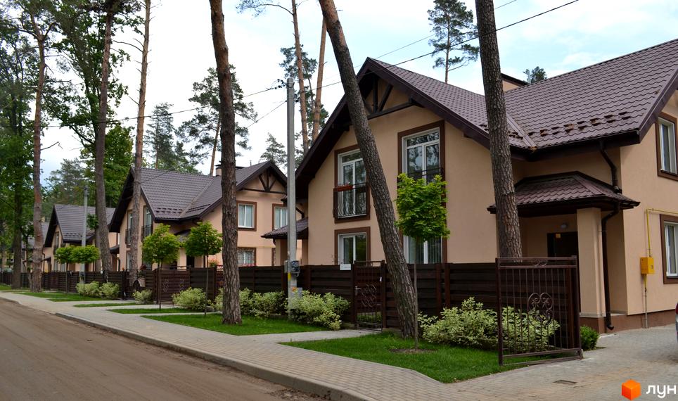 Котеджне містечко Sweet Home: ряд будинків з бежевими фасадами та коричневими дахами. Прибудинкова територія з зеленими насадженнями та високими соснами.