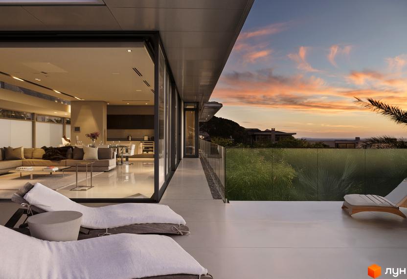 Фасад Комплексу Botanic Club House з панорамними вікнами та терасою. На терасі шезлонги, вид на зелені насадження та захід сонця над морем.