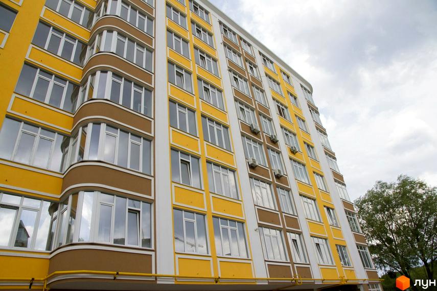 Багатоповерховий житловий будинок Житловий комплекс Єнісейська садиба з жовто-коричневим фасадом, білими вікнами та вигнутими балконами на фоні неба та дерев.