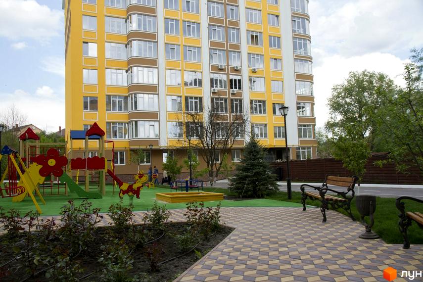 Житловий комплекс Єнісейська садиба: жовто-коричнева новобудова з дитячим майданчиком та лавками на прибудинковій території.