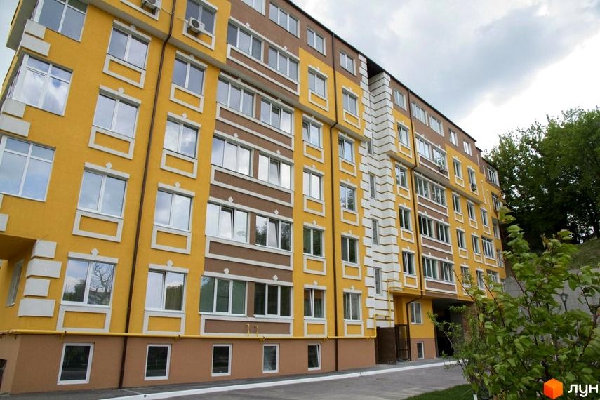 Новобудова ЖК Єнісейська садиба з жовто-коричневим фасадом та білими декоративними елементами. Поруч зелені дерева та кущі.