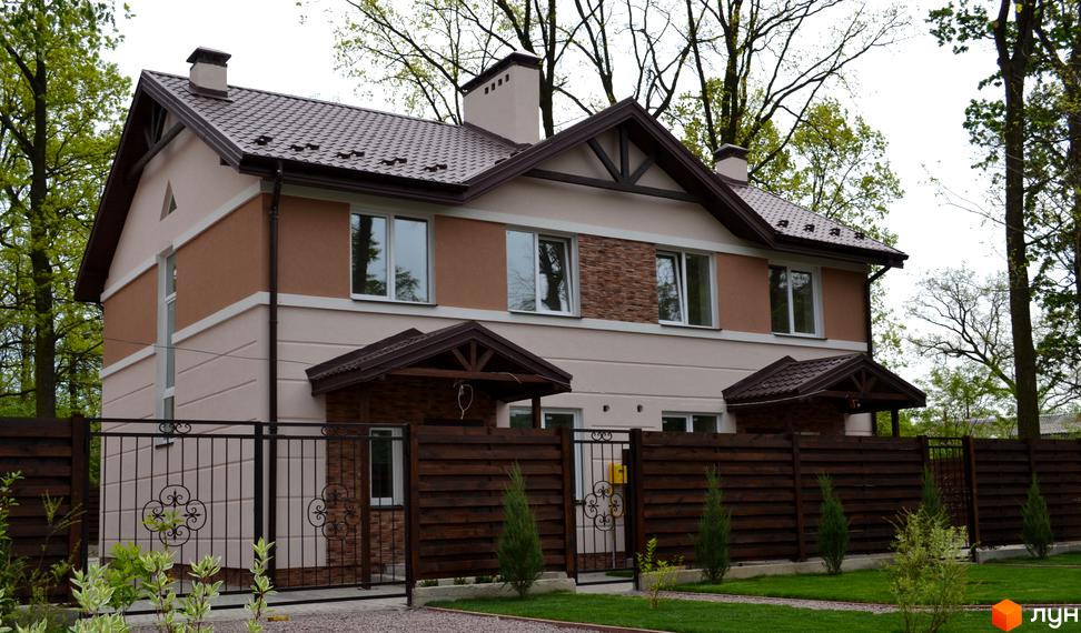 Будинок Котеджного містечка Sweet Home з бежево-коричневим фасадом, коричневим дахом та білими вікнами. Перед будинком доглянутий газон та дерев'яна огорожа з металевими воротами.