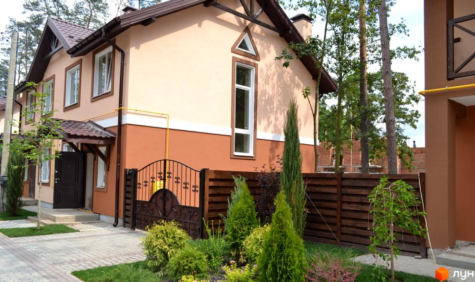 Котеджне містечко Sweet Home: двоповерховий будинок з бежевими та коричневими фасадами, коричневим дахом. Перед будинком доріжка з бруківки та доглянуті зелені насадження.