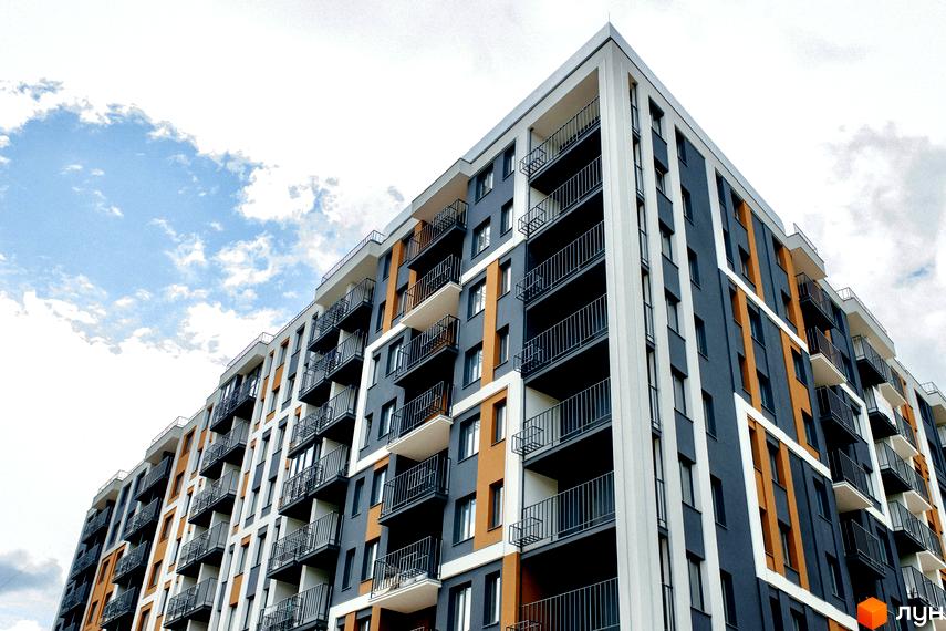 Житловий комплекс КЕЛЬЦЕ: багатоповерховий будинок з фасадом у сірих, білих та помаранчевих кольорах, обладнаний балконами з чорними поручнями.