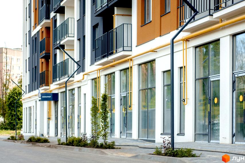 Зовнішній вигляд новобудови ЖК КЕЛЬЦЕ з великими вікнами та балконами, а також прибудинкова територія з деревами та тротуаром.