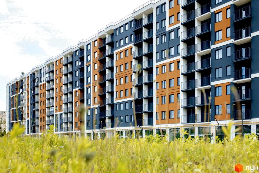 Новобудова ЖК КЕЛЬЦЕ з помаранчевими та синіми фасадами, балконами та зеленою травою на передньому плані.