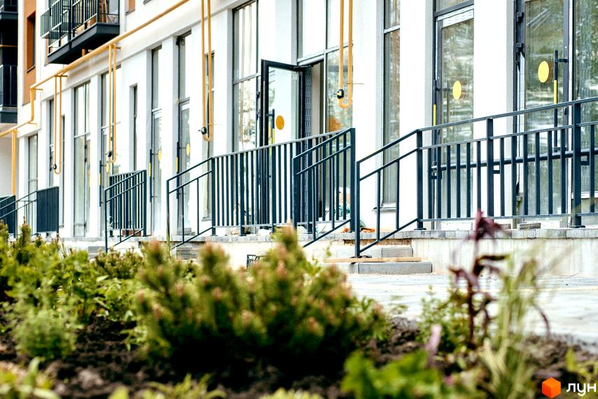 Житловий комплекс КЕЛЬЦЕ: фасади будівель з жовтими трубами та чорними перилами, перед ними зелені насадження.