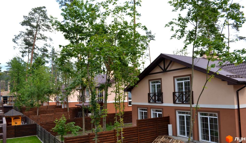 Будинки Котеджного містечка Sweet Home: бежево-коричневі фасади, коричневі дахи, білі вікна. Прибудинкова територія з деревами та дерев'яним парканом.