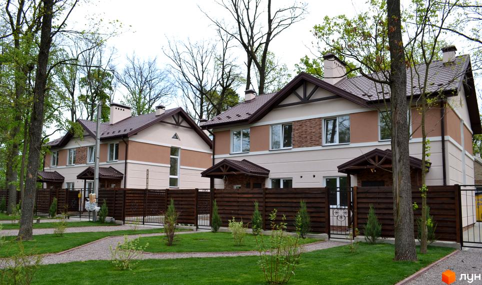 Двоповерхові будинки Котеджного містечка Sweet Home з коричневими дахами, світлими фасадами та декоративним оздобленням, оточені зеленими газонами та деревами.