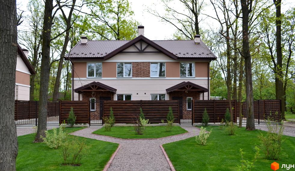 Двоповерховий будинок Котеджного містечка Sweet Home з коричневим дахом та світлим фасадом. Перед ним доглянутий газон, гравійні доріжки та дерев'яний паркан.