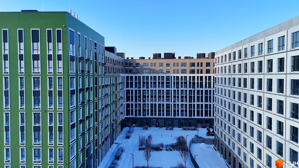 Житловий комплекс PARK ROYAL з зеленими та білими фасадами, вікнами та балконами, на тлі блакитного неба. На прибудинковій території взимку видно сніг, дерева та ліхтарі.