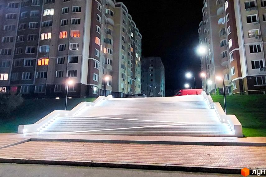 Житловий комплекс Дім у моря з підсвіченими сходами вночі. Сучасна архітектура багатоповерхових будинків та освітлена прибудинкова територія.