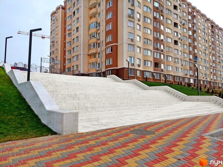 Новобудова ЖК Дім у моря з багатоповерховим будинком та великими сходами, що ведуть до нього. Територія навколо будинку упорядкована.