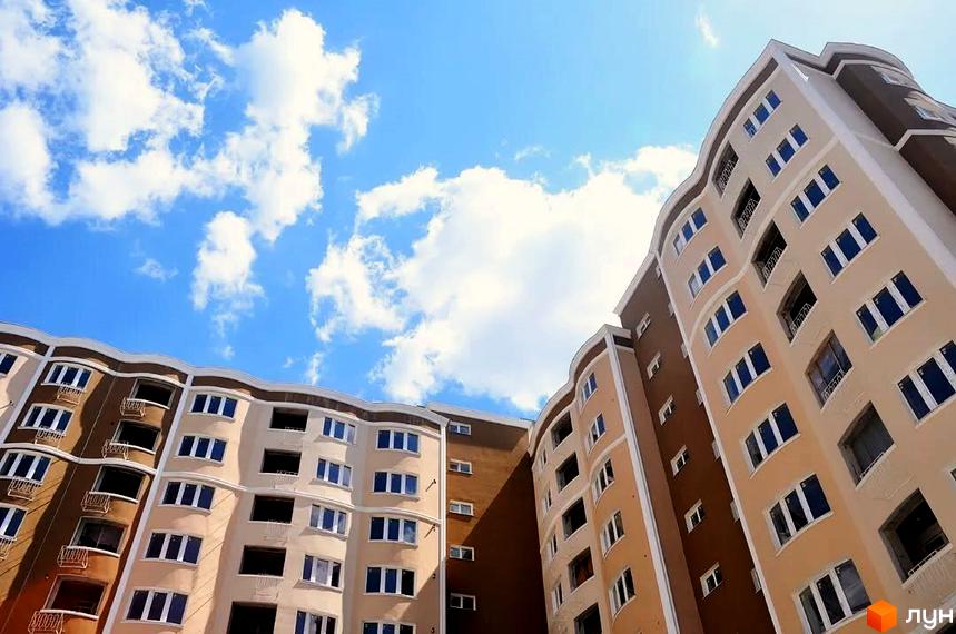 Зовнішній вигляд житлового комплексу Дім у моря з коричневими та бежевими фасадами та блакитним небом з хмарами. Новобудова з багатьма вікнами.