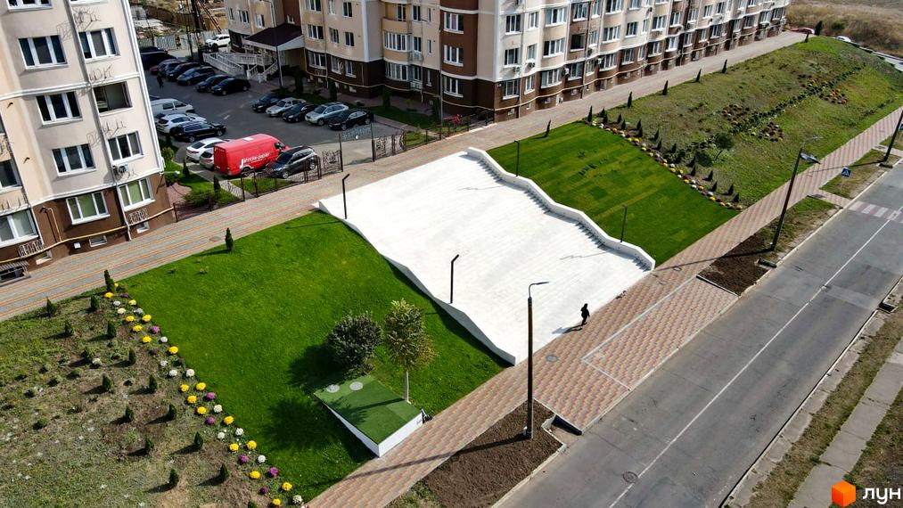 Житловий комплекс Дім у моря: багатоповерхові будинки з коричневими та бежевими фасадами, прибудинкова територія з доглянутими газонами, квітковими клумбами та пішохідними доріжками.