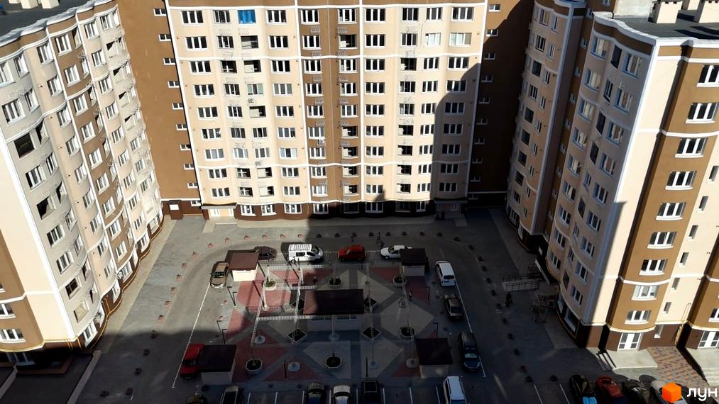 Житловий комплекс Дім у моря: багатоповерхові будинки з бежевими та коричневими фасадами, вікнами та прибудинковою територією з парковкою та зеленими зонами.