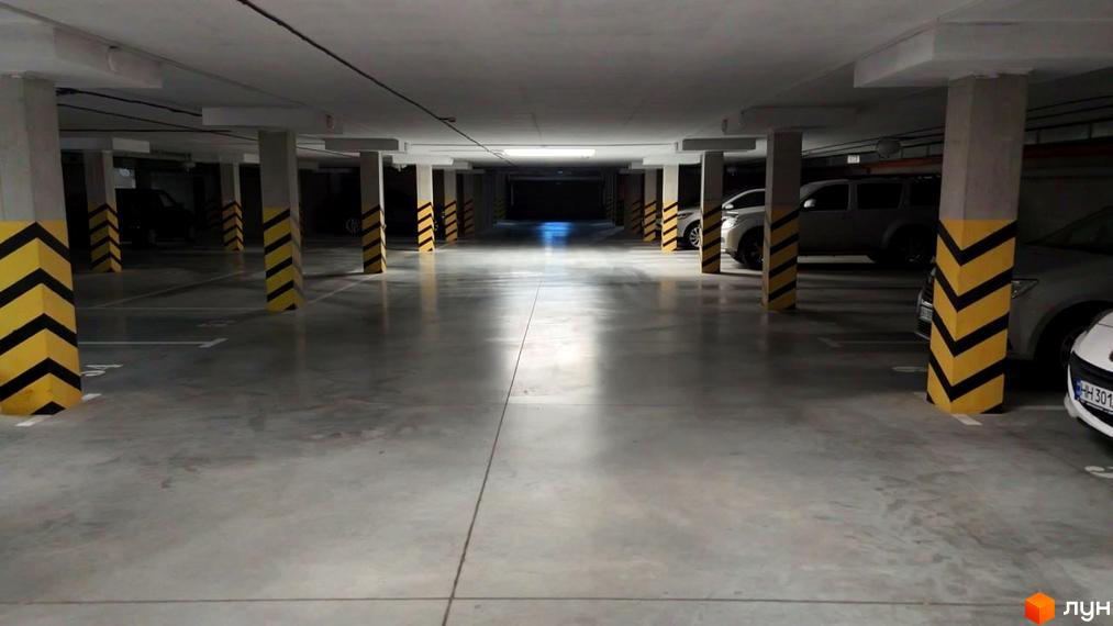 Підземний паркінг ЖК Дім у моря з колонами, розміченими паркувальними місцями та автомобілями. Просторий бетонний майданчик для паркування.