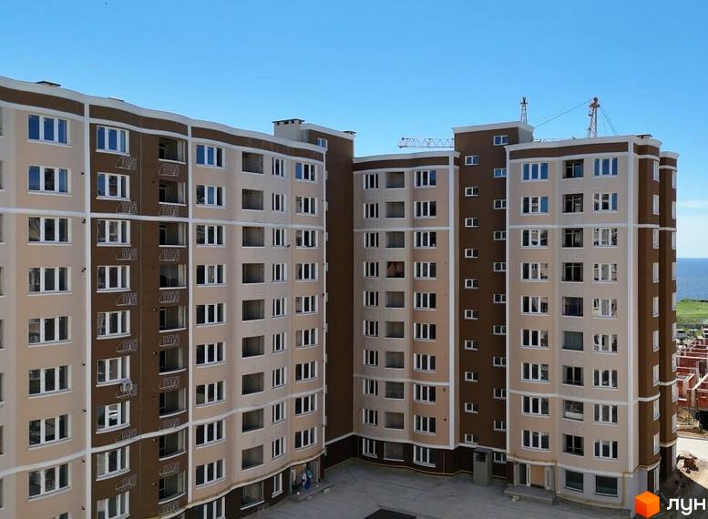 Будівельний проєкт Дім у моря: багатоповерхові будинки з коричневими та бежевими фасадами, вікнами та балконами, на фоні блакитного неба та моря.