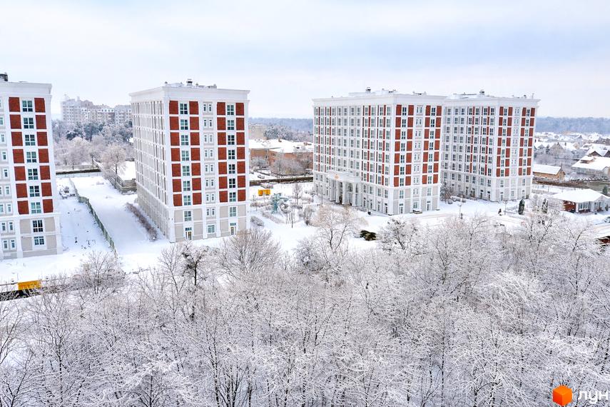 Житловий комплекс OXFORD у зимовому вбранні, з білими будівлями та червоними елементами, оточений засніженими деревами та доглянутою територією.