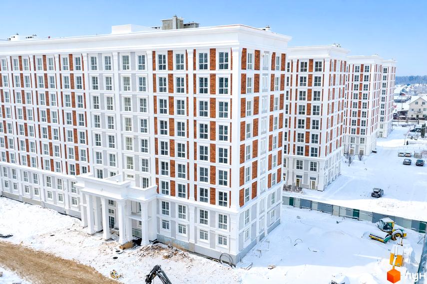 Зовнішній вигляд житлового комплексу OXFORD з білими фасадами та цегляними вставками, на тлі засніженої території та блакитного неба.