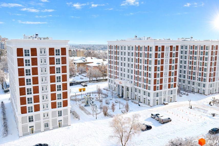 Житловий комплекс OXFORD у зимовий період, з білими фасадами та цегляними вставками, на тлі засніженої території з дитячим майданчиком.