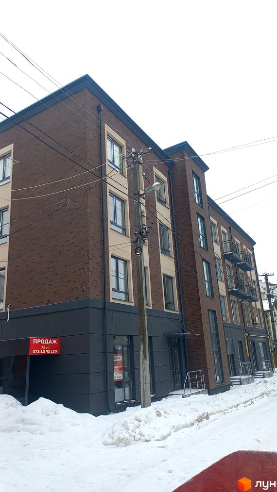 Зовнішній вигляд новобудови з коричневої цегли та світлої штукатурки, з балконами та вікнами, на тлі засніженої вулиці. Будинок розташований за адресою вул. Вагилевича, 9.