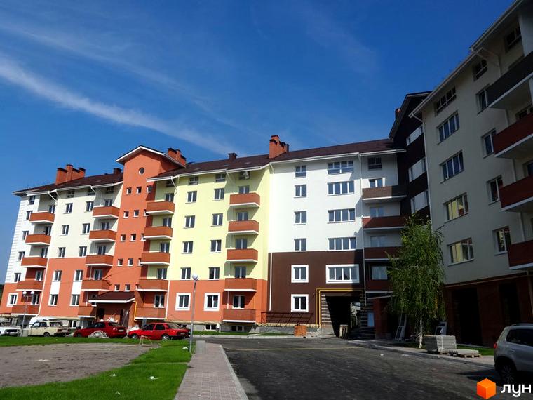 Житловий комплекс Хотів: багатоповерховий будинок з фасадами білого, помаранчевого, жовтого та коричневого кольорів. Прибудинкова територія з дорогою та зеленою зоною.