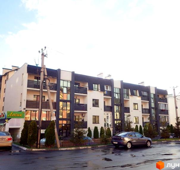 Зовнішній вигляд новобудови на вулиці Щаслива. Прибудинкова територія з деревами та припаркованими автомобілями.