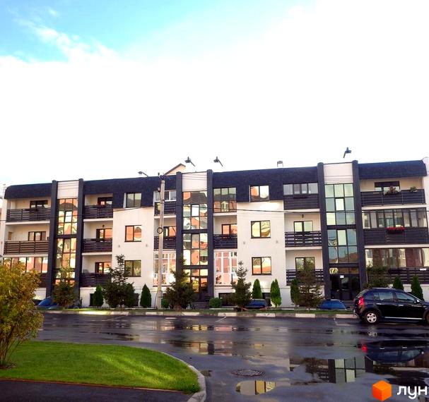 Зовнішній вигляд житлового комплексу на вул. Щаслива з великими вікнами та балконами, зелена прибудинкова територія з деревами та автомобілями.