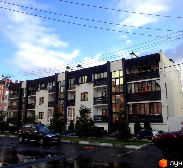 Зовнішній вигляд новобудови на вул. Щаслива, з балконами та великими вікнами. Прибудинкова територія з деревами та припаркованими автомобілями.