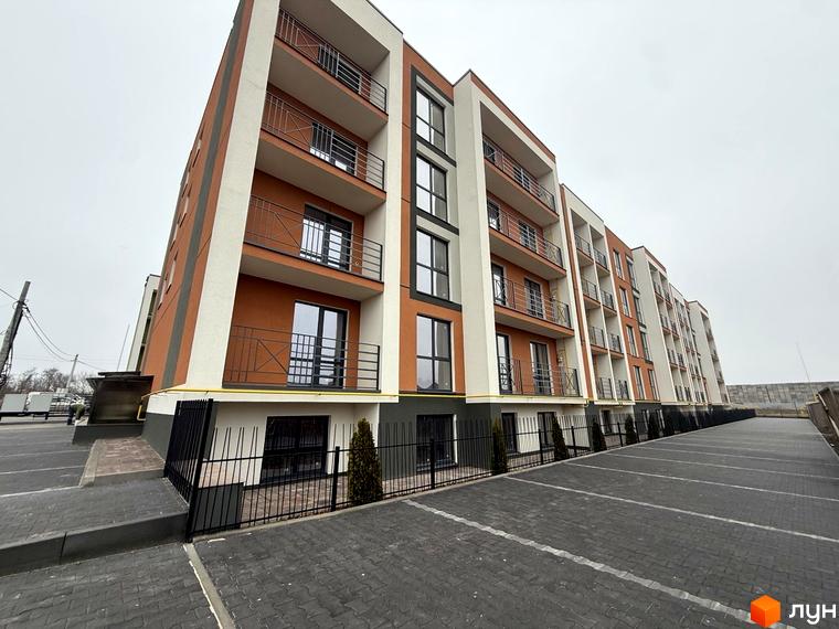 Новобудова Brickwood 2 з оранжевими та білими фасадами, балконами та парковкою. Прибудинкова територія з бруківкою та огорожею.