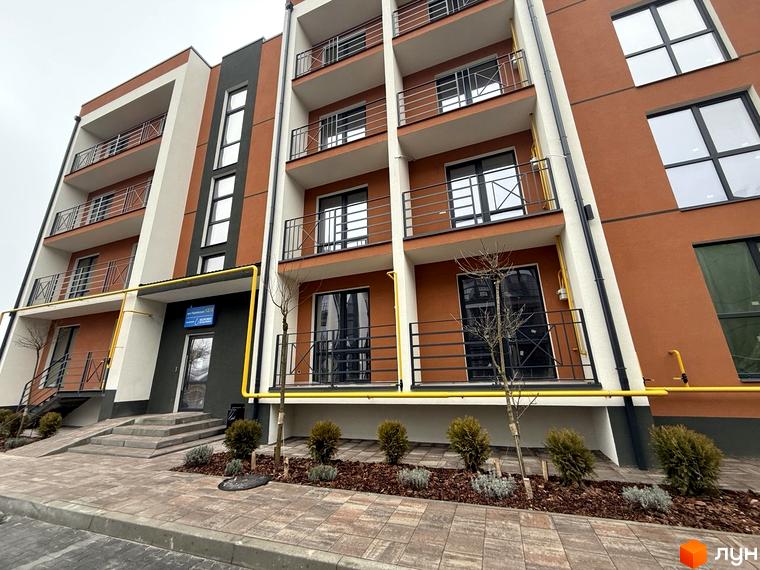 Житловий комплекс Brickwood 2: багатоповерховий будинок з помаранчевим фасадом, балконами. Прибудинкова територія з бруківкою, молодими деревами та кущами.