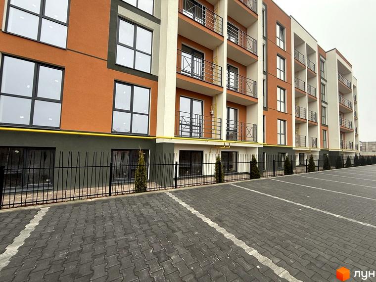 Житловий комплекс Brickwood 2 має багатоповерховий будинок з помаранчевим та темно-сірим фасадом, балконами та великими вікнами. Прибудинкова територія облаштована парковкою з бруківки та огорожею з декоративними кущами.