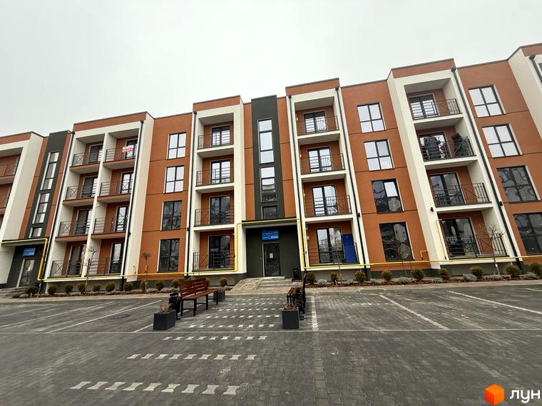 Житловий комплекс Brickwood 2: багатоповерховий будинок з фасадом теракотового та білого кольорів, балконами. Перед будинком парковка та лавки.