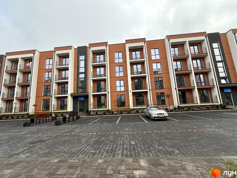 Житловий комплекс Brickwood 2: багатоповерховий будинок з помаранчевим, білим та темно-сірим фасадом. Перед ним розташований вимощений паркінг з лавками та озелененням.