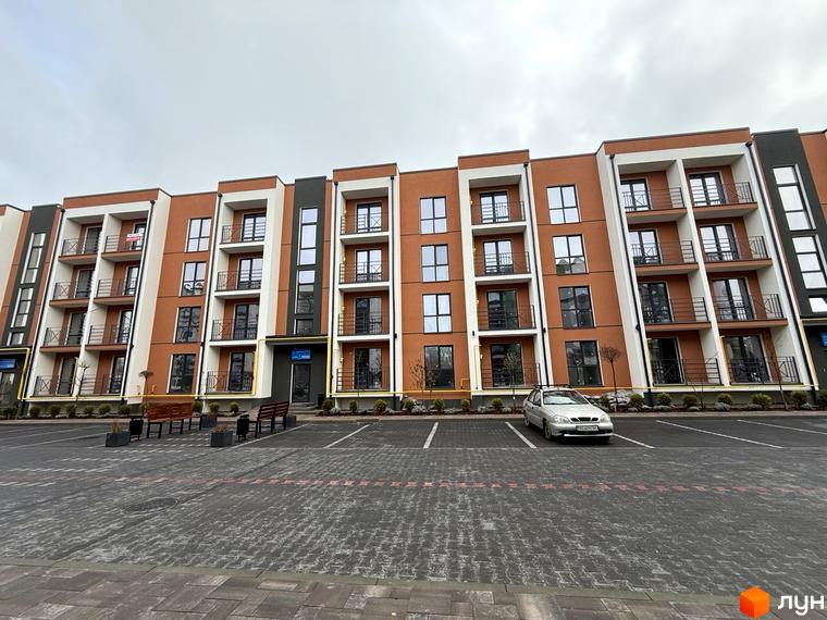 Житловий комплекс Brickwood 2 з багатоповерховим будинком у коричневих, білих та темно-сірих тонах. Перед ним розташований паркінг та озеленена прибудинкова територія.