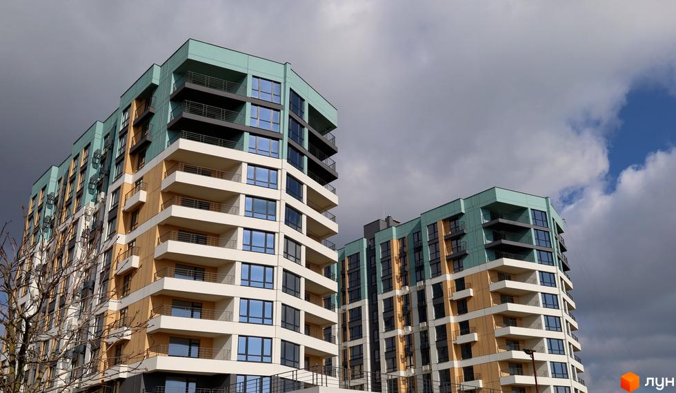 Житловий комплекс Парус. Дві багатоповерхові будівлі з бірюзовими, жовтими та білими фасадами, численними балконами під хмарним небом.
