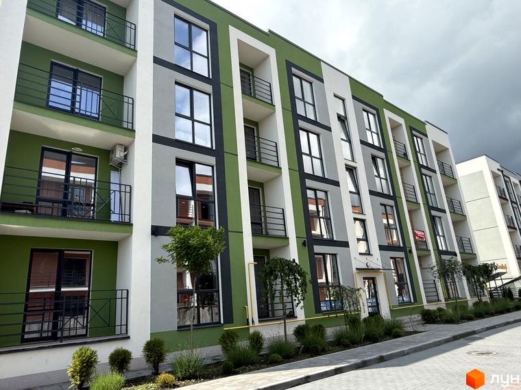 Фасад Житлового комплексу Brickwood 2 з зеленими, сірими та білими секціями, балконами та вікнами. Прибудинкова територія з доріжкою та рослинами.