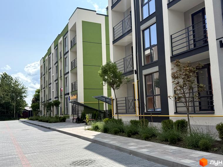 Новобудова Brickwood 2: багатоповерховий будинок із зеленим та білим фасадом, балконами. Прибудинкова територія має мощені доріжки та зелені насадження.