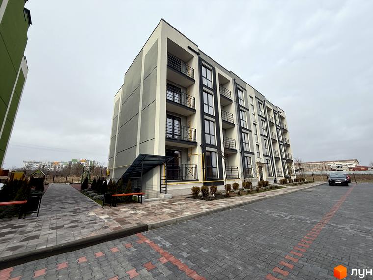 Новобудова Brickwood 2 з балконами та паркуванням. Поруч доглянута прибудинкова територія з лавками та доріжками.