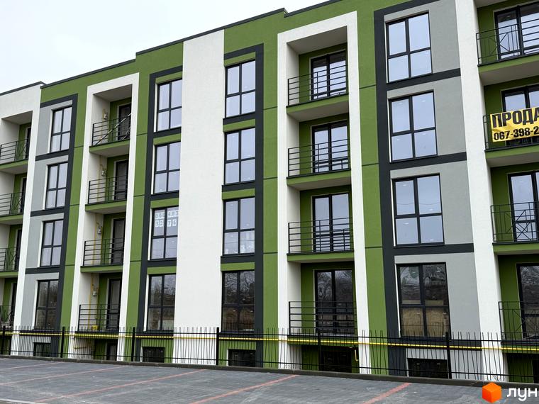 Фасад новобудови ЖК Brickwood 2 з зеленими та білими елементами, балконами та великими вікнами. Поруч розташована парковка та огорожа.