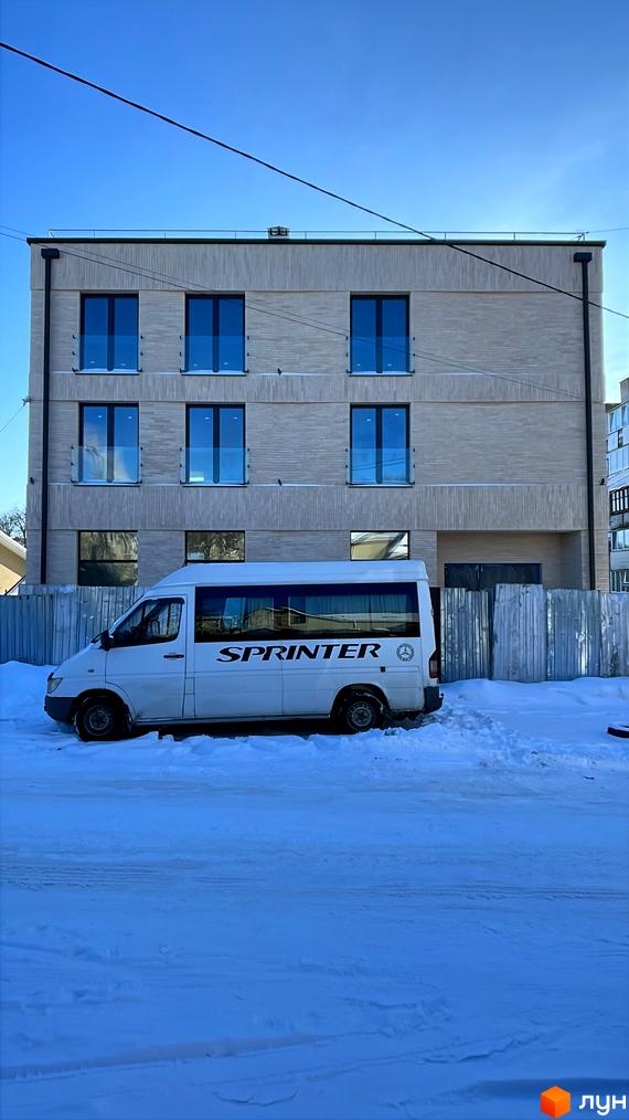 Триповерховий Житловий комплекс світлого кольору з темними вікнами та скляними балконами. Перед будинком засніжена територія.