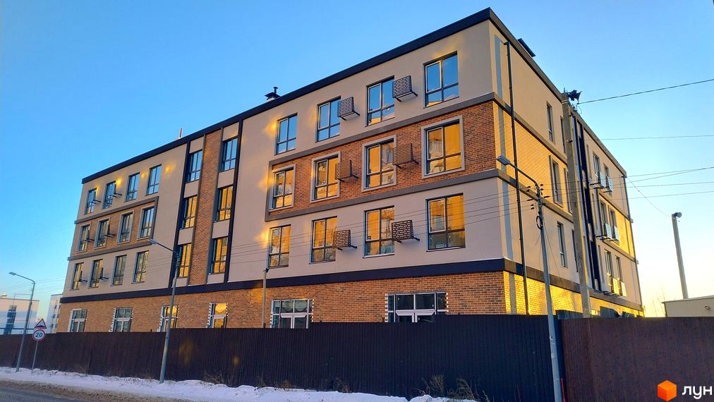 Новобудова Europian Residences з цегляним фасадом та великими вікнами на тлі блакитного неба. Огороджена територія з парканом та засніженою дорогою.