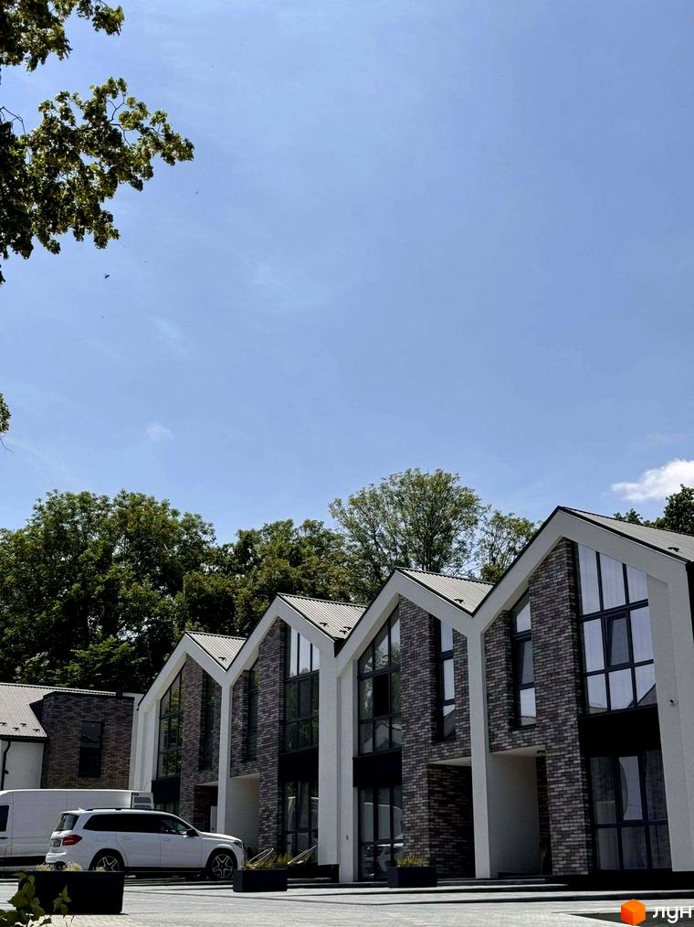Котеджне містечко КМ Linden Park: фасади будинків з цегли та великими вікнами, поряд зелені дерева та авто.
